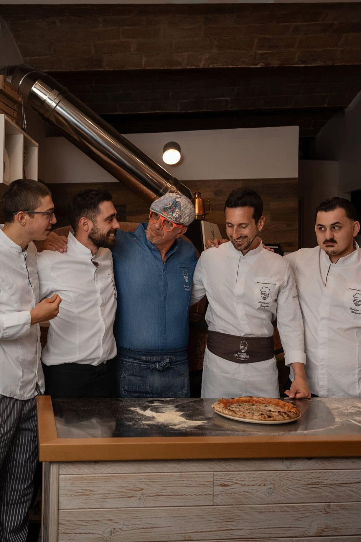 Giovanni Santarpia con camicia blu insieme al suo staff dietro il bancone della pizzeria.