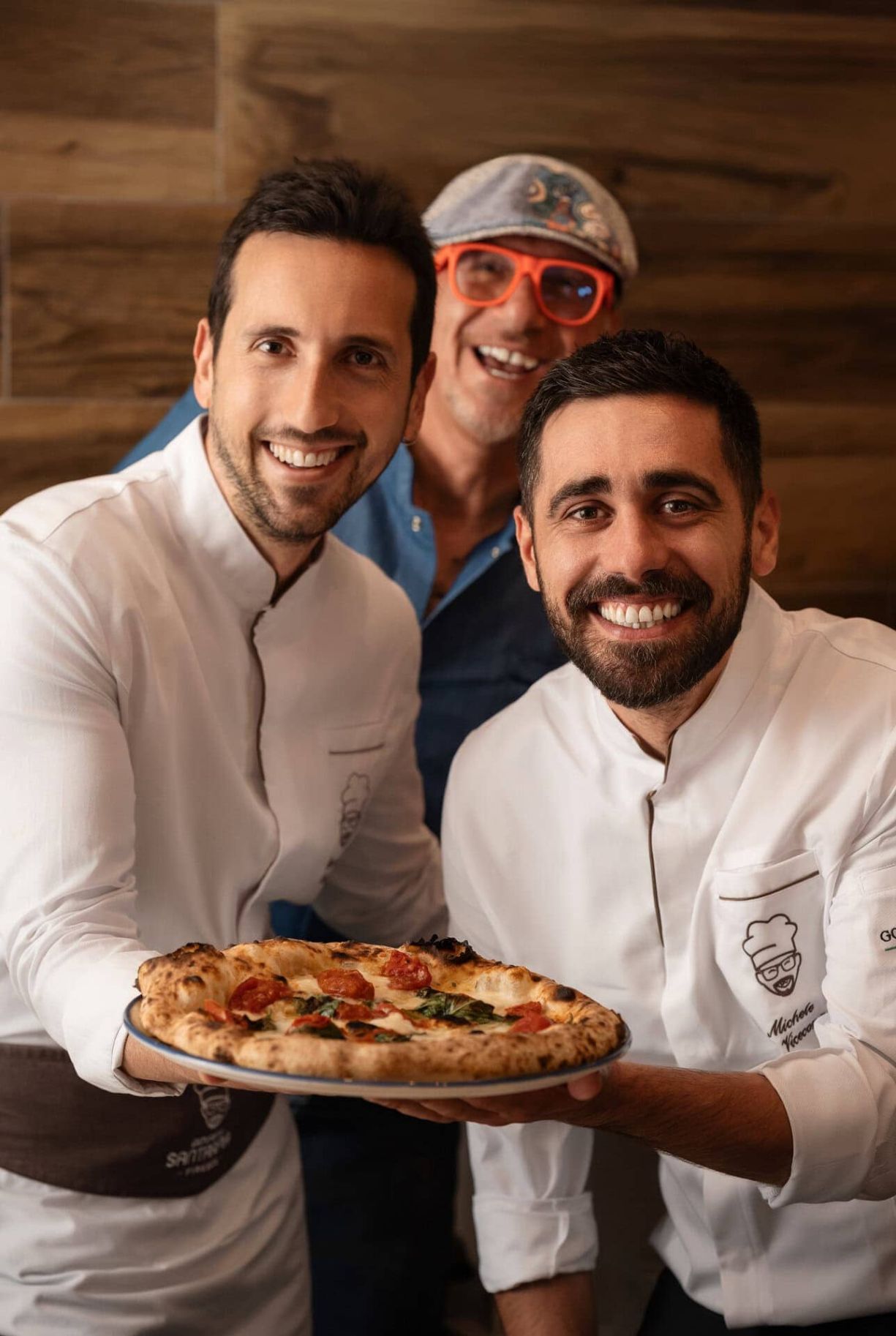 Giovanni e il suo team che sorridono alla fotocamera mentre presentano una pizza appena sfornata.